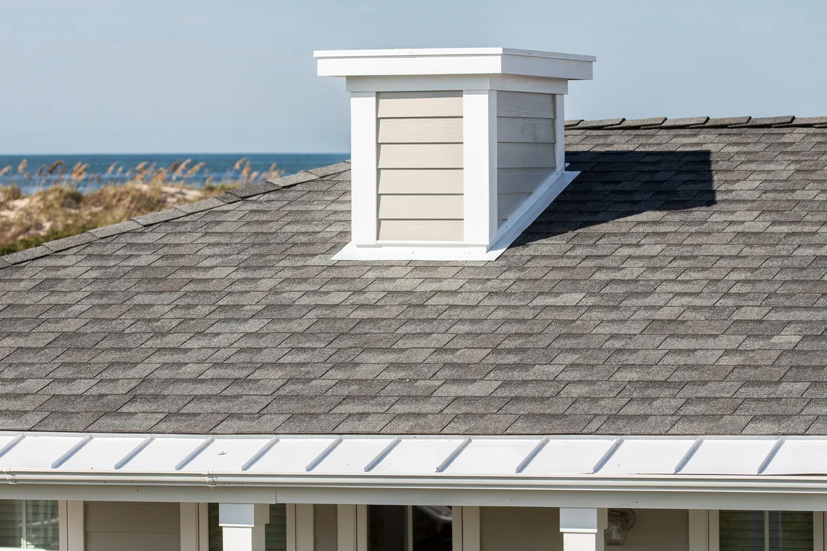A new grey shingle roof meeting a white dormer on a coastal home